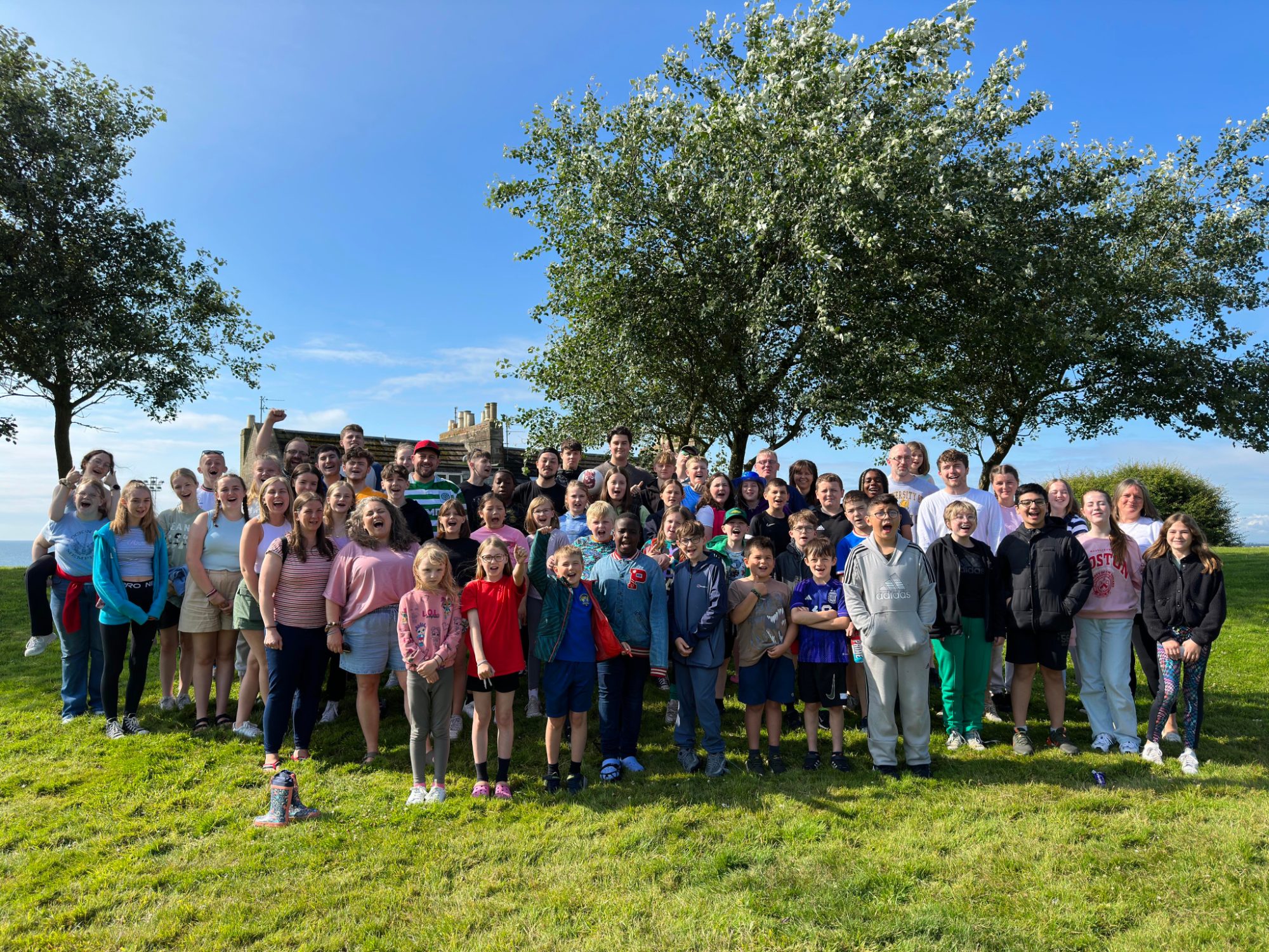 A large group of children, young people and leaders standing together on the grass at district summer camp